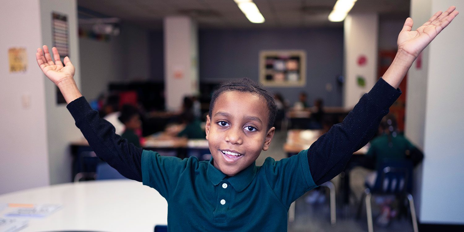 Smiling student with his hands up in class